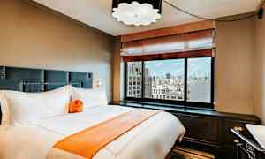 Ett elegant hotellrum med en säng, stora fönster och stadsvy. (AI-genererad text)