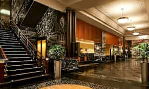 Bild på en hotellets lobby med marmorgolv, en trappa, soffor och växtarrangemang. (AI-genererad text)