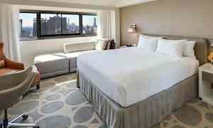 Ett hotellrum med en stor säng och utsikt mot staden genom fönstret. (AI-genererad text)