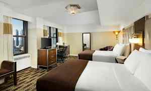 Ett hotellrum med två dubbelsängar, skrivbord, TV och två stora fönster. (AI-genererad text)