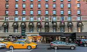 En byggnad i tegel med markiser över entréer, trafik med bilar och taxibilar på gatan. (AI-genererad text)