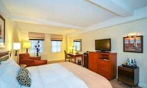 Ett hotellrum med en stor säng, en fåtölj, ett skrivbord och en TV på en byrå. (AI-genererad text)