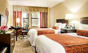 Hotelrum med två enkelsängar, ett skrivbord med stol samt en lampa och fönster som vetter mot staden. (AI-genererad text)