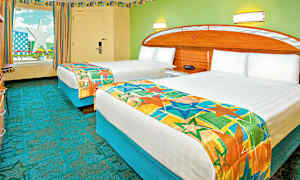 Ett hotellrum med två enkelsängar täckta med färgglada sängöverkast. Väggarna är målade i grönt och det finns ett fönster med utsikt mot en stjärnformad konstruktion. (AI-genererad text)