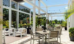 En utomhus lounge med vita möbler och gröna växter, täckt av ett pergolatak. (AI-genererad text)