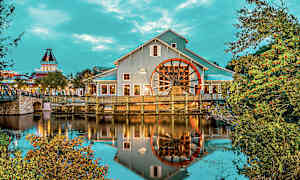 Byggnad med ett stort hjul vid vatten, omgiven av träd och grönska. (AI-genererad text)