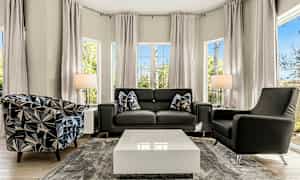 Ett modernt vardagsrum med en soffa och två fåtöljer, ett soffbord i mitten och stora fönster som släpper in naturligt ljus. (AI-genererad text)