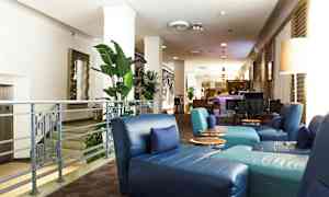 Bild av en hotellobby med blå sittstolar, gröna växter och en bar i bakgrunden. (AI-genererad text)