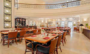 Elegant restaurang med bord och stolar i trä, dekorerat med röda servetter och blommor. Bar och ljus inredning syns i bakgrunden. (AI-genererad text)