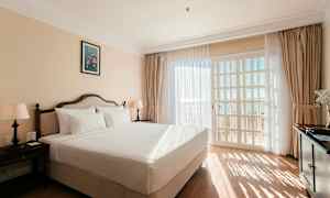 Ett ljust hotellrum med en dubbelsäng, två nattduksbord med lampor och en stor fönsterdörr med utsikt. (AI-genererad text)