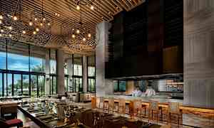 Interiör av en modern restaurang med stora fönster, upplyst takdekoration och en bardisk där två kockar arbetar. (AI-genererad text)