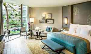 Ett elegant hotellrum med en stor säng, en sittgrupp och ett stort fönster med utsikt över palmträd och en pool. (AI-genererad text)