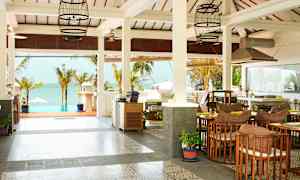 En öppen och ljus miljö vid kusten med palmer, bord och stolar samt utsikt över havet. (AI-genererad text)