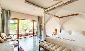 Ett hotellrum med en himmelssäng och en balkong i bakgrunden. (AI-genererad text)