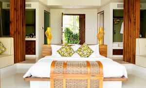 Ett sovrum med en dubbelsäng, prydd med gröna dekorationskuddar. Rummet har trädetaljer och syns med öppna dörrar som leder ut mot grönska. (AI-genererad text)