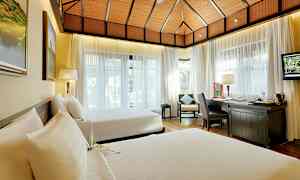 Ett hotellrum med två sängar, stora fönster med ljusa gardiner och en arbetsyta med skrivbord och stol. (AI-genererad text)