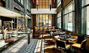 Interiör av en modern restaurang med bord och stolar, stora fönster och ett öppet köksområde. (AI-genererad text)