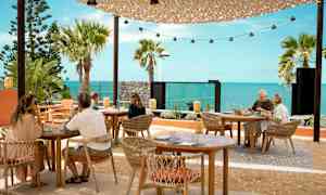 Uteservering med bord och stolar framför en havsutsikt. (AI-genererad text)