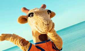 Maskot giraff vid stranden. (AI-genererad text)