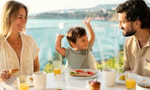 En familj äter frukost vid ett bord med utsikt över havet. (AI-genererad text)