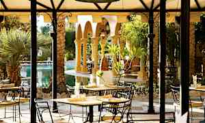 En utomhusrestaurang vid en pool med palmer och valv. (AI-genererad text)