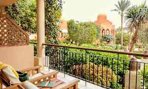 Ett uterum med möbler framför en frodig trädgård och en byggnad med kupol. (AI-genererad text)