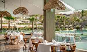 Restaurang med bord klädda i vita dukar och utsikt över pool och palmer. (AI-genererad text)