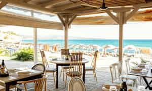 Uteservering med utsikt över havet och en strand med solstolar. (AI-genererad text)