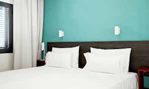 Hotellrum med en bäddad säng med vita lakan och blå vägg. (AI-genererad text)