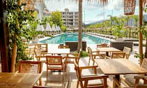 Bild av ett hotellområde med solstolar bredvid en rektangulär pool och träbord i förgrunden. (AI-genererad text)