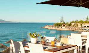 Utsikt över havet från en restaurangterrass med vita bord och stolar. (AI-genererad text)