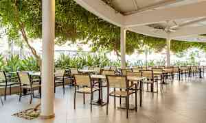 Bild av en utomhusrestaurang med bord och stolar under tak. (AI-genererad text)