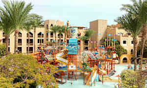 Bild på en vattenpark med rutschbanor och lekställningar, omgiven av palmer och hotellbyggnader. (AI-genererad text)