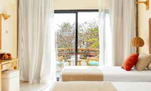 Ett hotellrum med dubbelsängar och en glasdörr som leder ut till en balkong. (AI-genererad text)