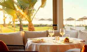 En dukad restaurang med mat och glas vid en solig utsikt med palmer. (AI-genererad text)