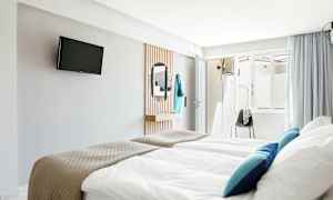 Hotellrum med sängar, TV på väggen, och en spegel. (AI-genererad text)