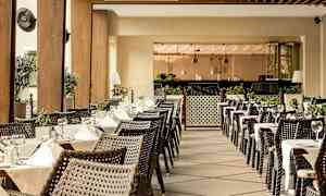 Uteservering med dukade bord och korgstolar, omgiven av grönska och modern inredning. (AI-genererad text)