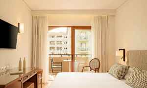 Modernt hotellrum med dubbelsäng, skrivbord, TV och balkong med utsikt. (AI-genererad text)