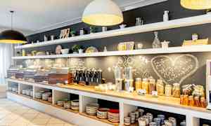 Frukostbuffé med bröd, flingor, pålägg och drycker. Hyllor med porslin ovanför. (AI-genererad text)