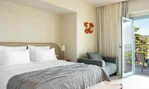 Hotelrum med bäddad säng, fåtölj och öppen balkongdörr. (AI-genererad text)