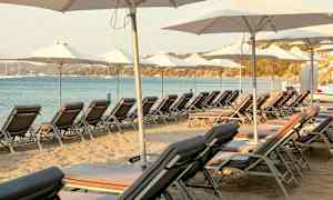 Solstolar och parasoller uppställda på sandstrand vid havet. (AI-genererad text)