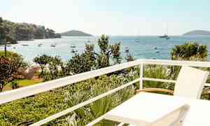 Utsikt från en balkong över havet med båtar och grönska. (AI-genererad text)