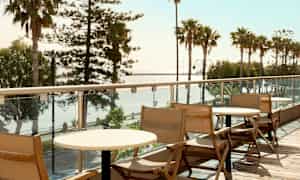 Trästolar och bord på en balkong med utsikt över palmer och hav. (AI-genererad text)