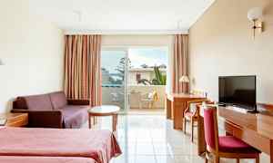 Ett hotellrum med två sängar, en soffa, ett bord, ett skrivbord med stol och en balkong med utsikt. (AI-genererad text)