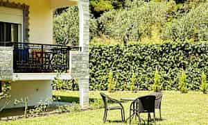 En grön trädgård med ett bord och stolar på gräset, intill en balkong. (AI-genererad text)