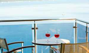 Två glas med röd dryck på ett bord på en balkong med utsikt över havet. (AI-genererad text)