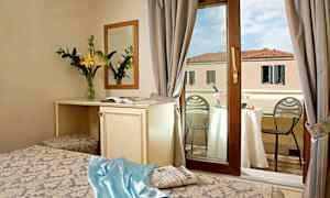 Hotellrum med fönster mot en balkong, bord med champagne och utsikt över byggnad. (AI-genererad text)