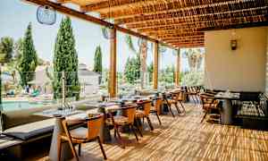 Restaurangutomhusterrass med bord och stolar, med utsikt över en pool och träd. (AI-genererad text)