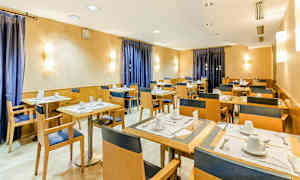 Ett matsalsutrymme med uppsatta bord och stolar, väggar med varma toner och blå gardiner. (AI-genererad text)