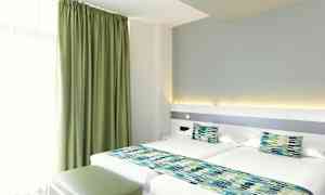 Ett hotellrum med två enkelsängar, gröna gardiner och matchande sängdekorationer. (AI-genererad text)